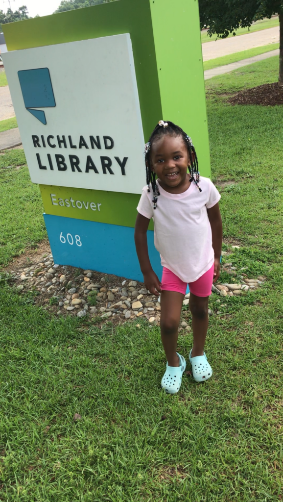 Toddler standing by Richland Library Eastover sign.